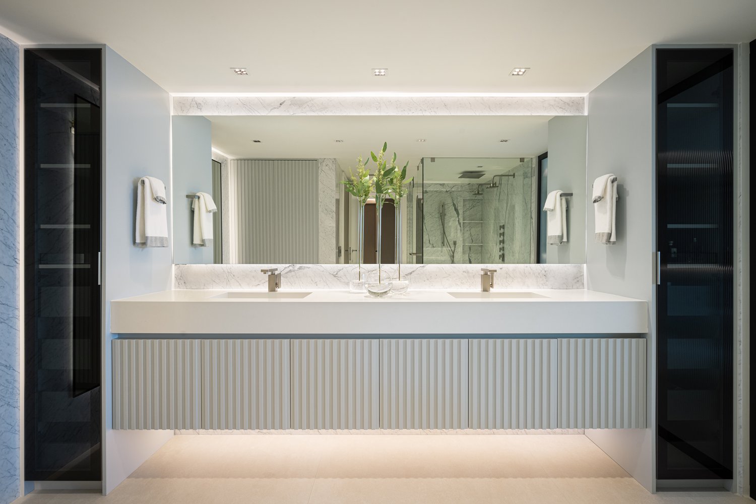 Master bath with fluted floating double vanity, marble backsplash and glass storage towers