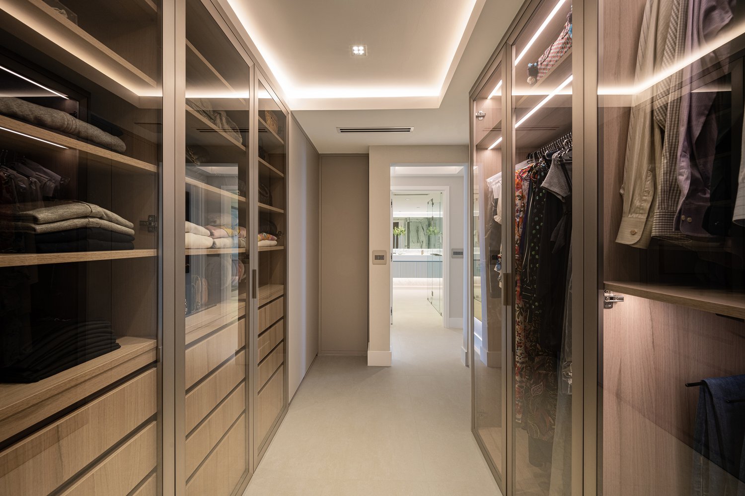 Glass-front walk-in closet hallway with lit wood shelving