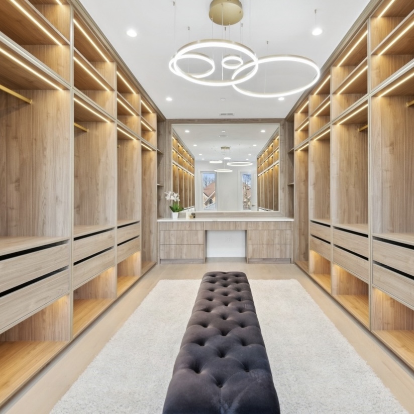 Oak walk-in closet suite with LED-lit shelving, ring chandeliers and tufted bench