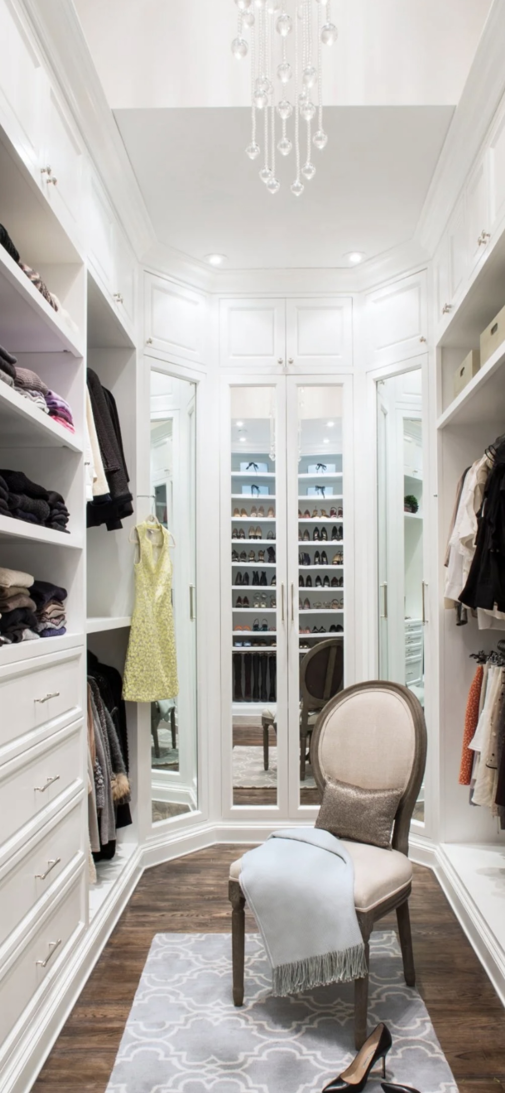 Classic white galley walk-in closet with mirrored doors, crystal chandelier and shoe display