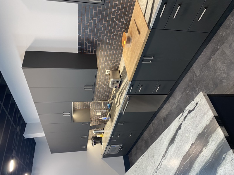 Commercial office break room kitchenette with dark cabinetry, waterfall marble island and subway tile backsplash