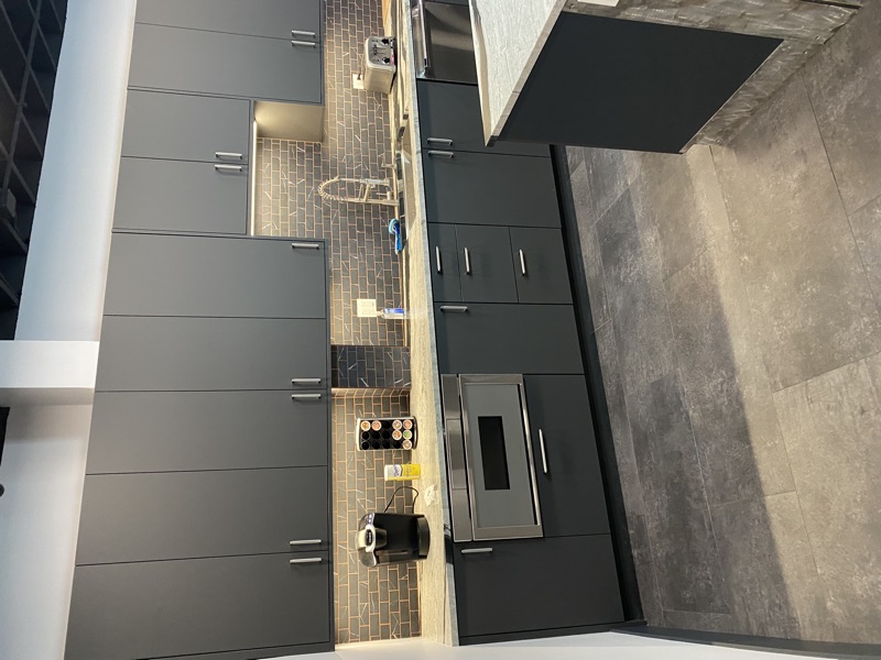 Wide view of commercial office break room with dark cabinetry and exposed ceiling