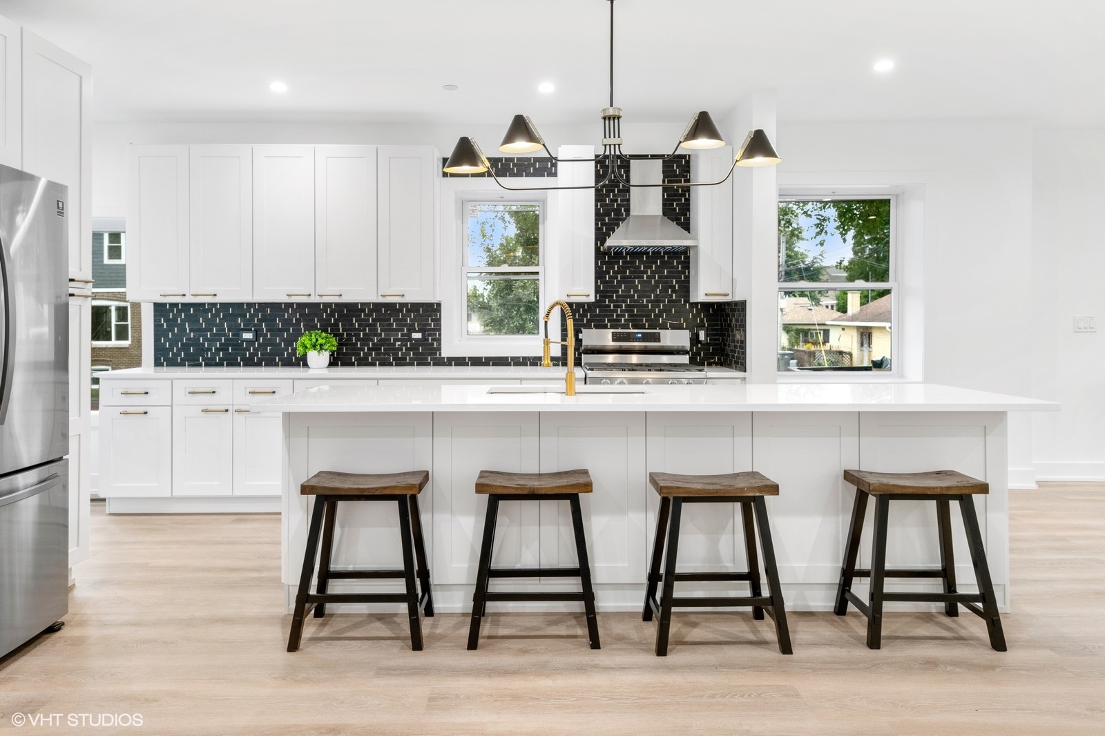 White kitchen with black subway tile backsplash, brass fixtures and waterfall island