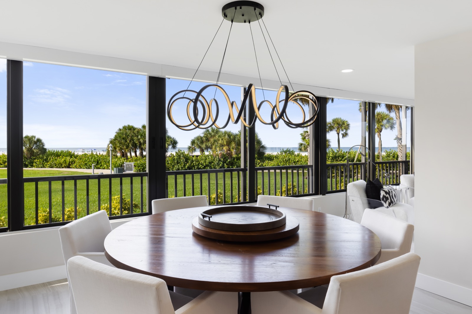 Round wood dining table beneath a swirling ring pendant chandelier with ocean view